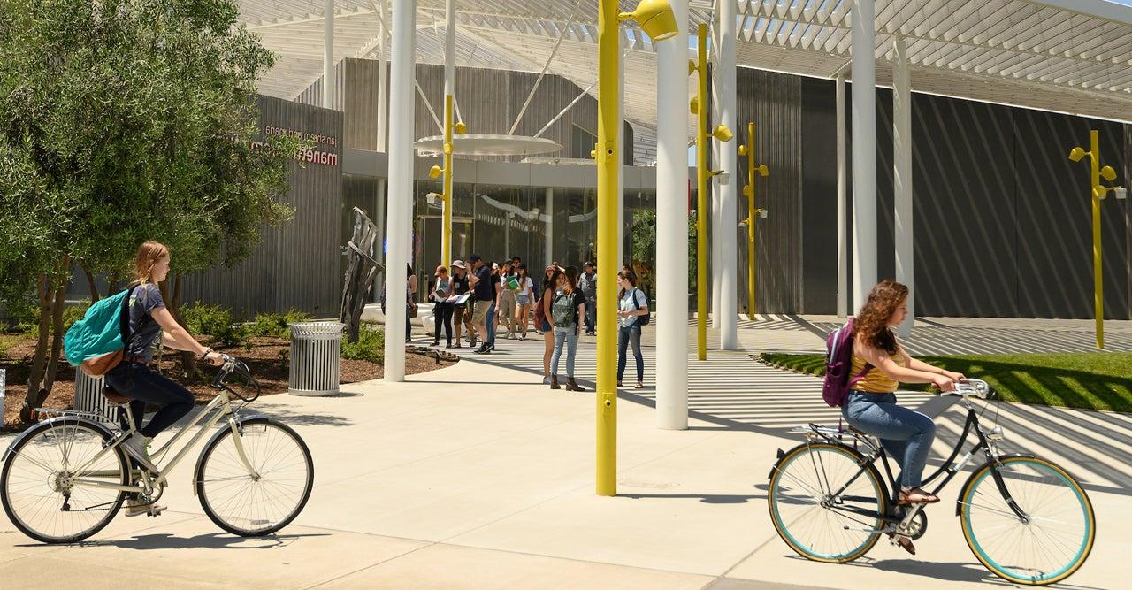 two students riding bikes in front of the Manetti Shrem museum