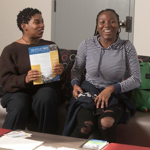 two females students laugh while studying on a couch