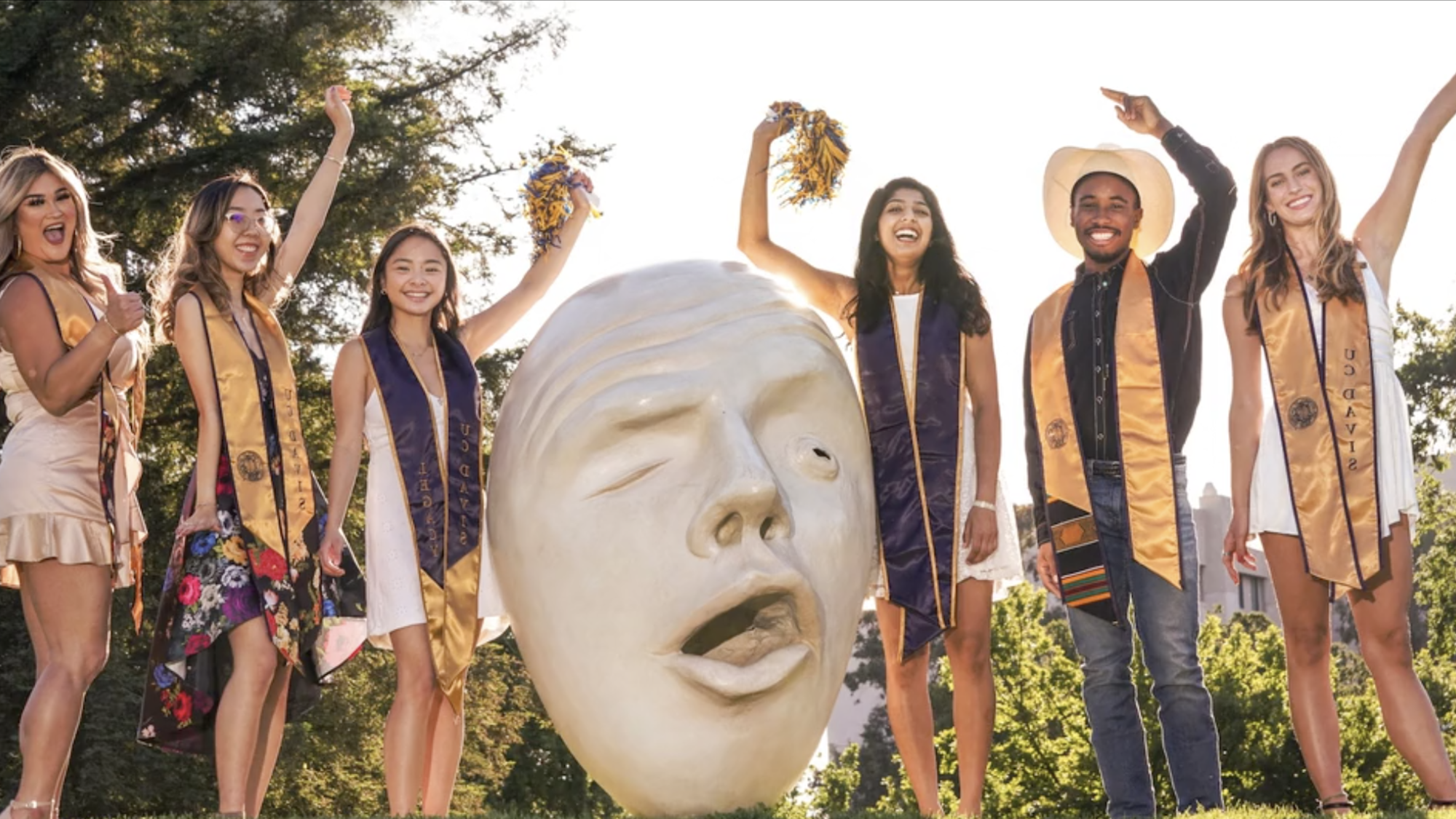six students in graduation hats and sashes pose near an Egghead statue at UC Davis