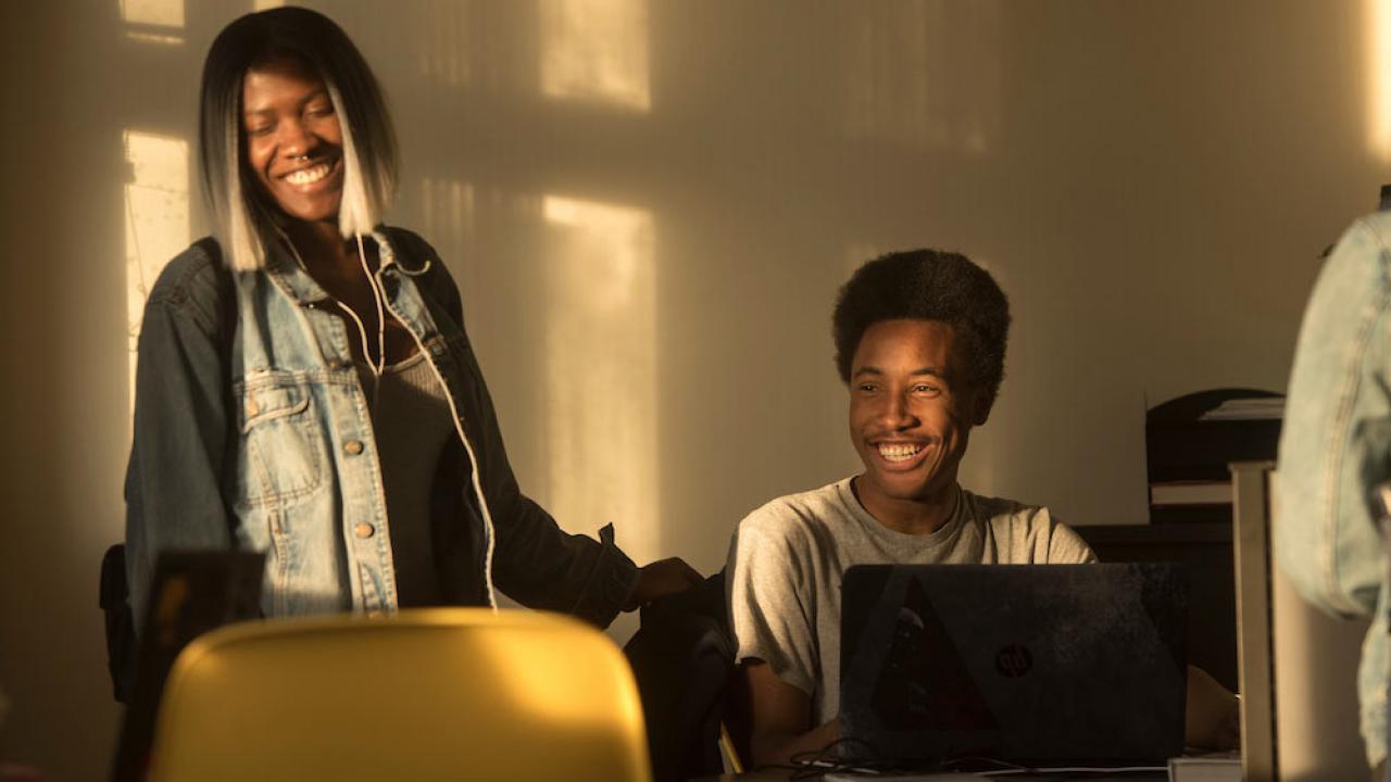 Two students laugh while collaborating on a project