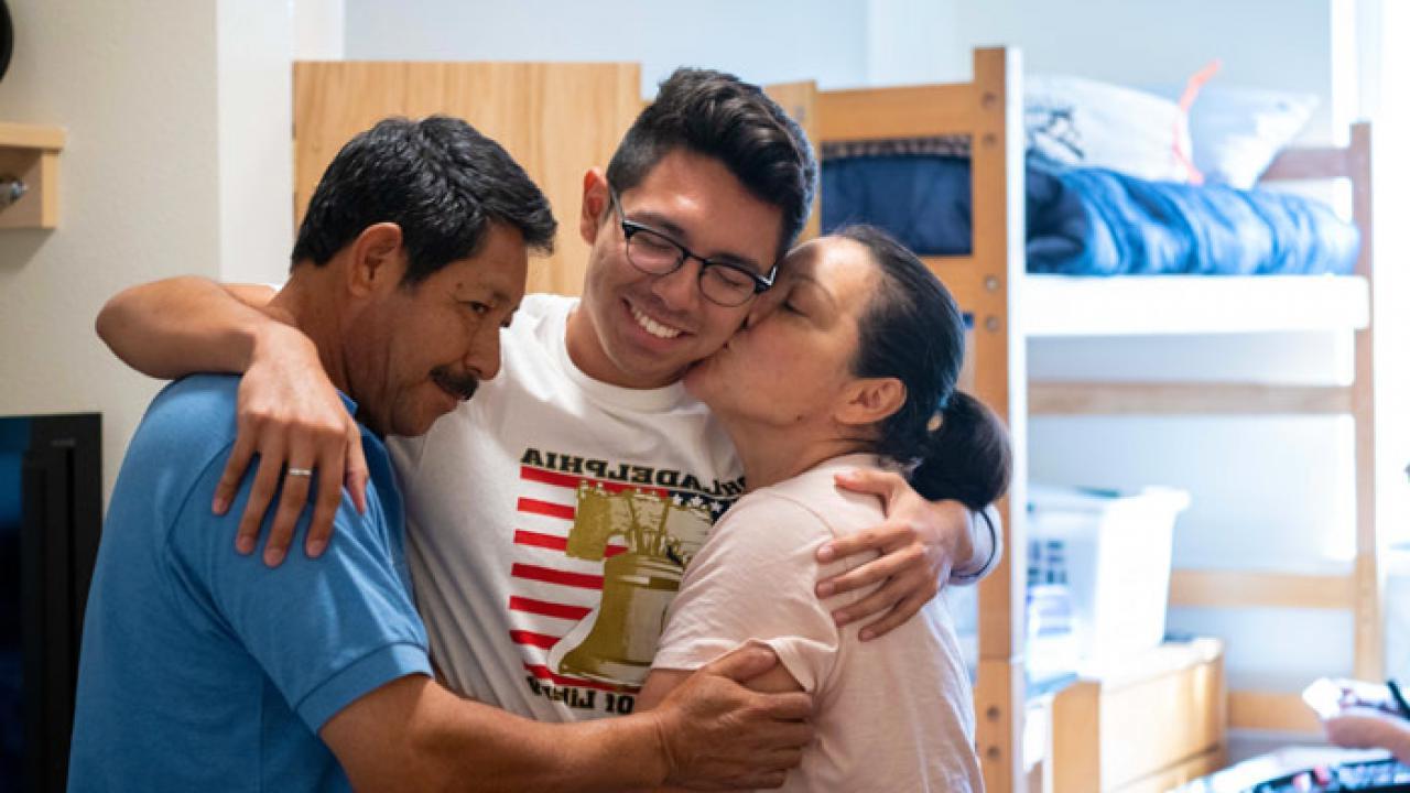 a student hugging his parents inside a residence hall room