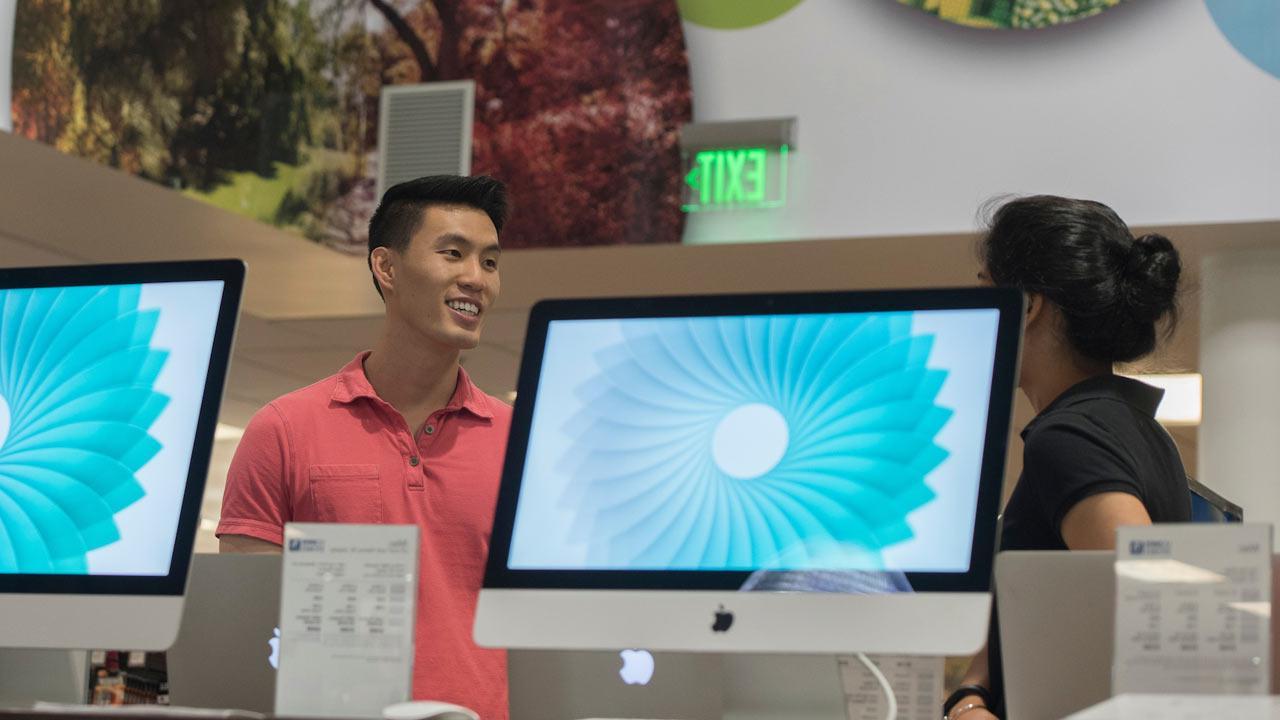 A UC Davis stores student staff member discusses computer options in the computer section of the flagship UC Davis store.