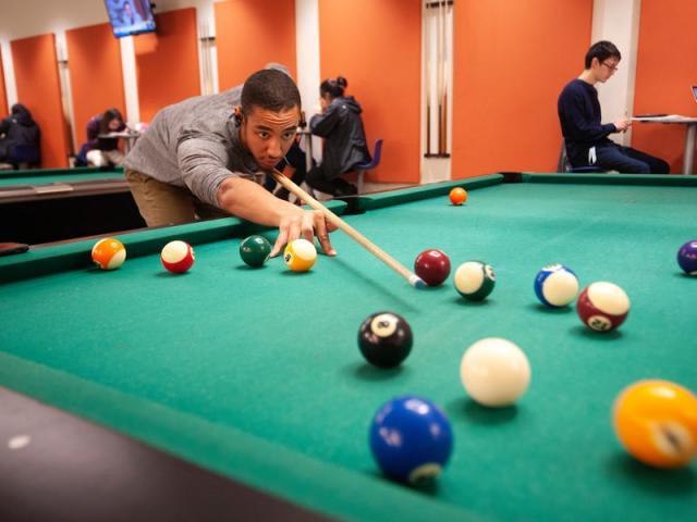 A male student lines up a pool shot on one of the MU games area tables