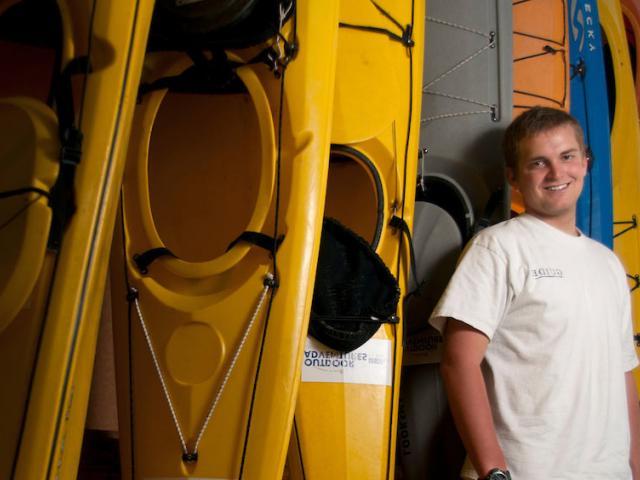 A male student stands in front of a stack of colorful kayaks