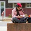 A student wearing a beret uses their smartphone outside of the UC Davis Craft Center.