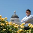 A student poses in front of the state capitol dome and yellow roses. 