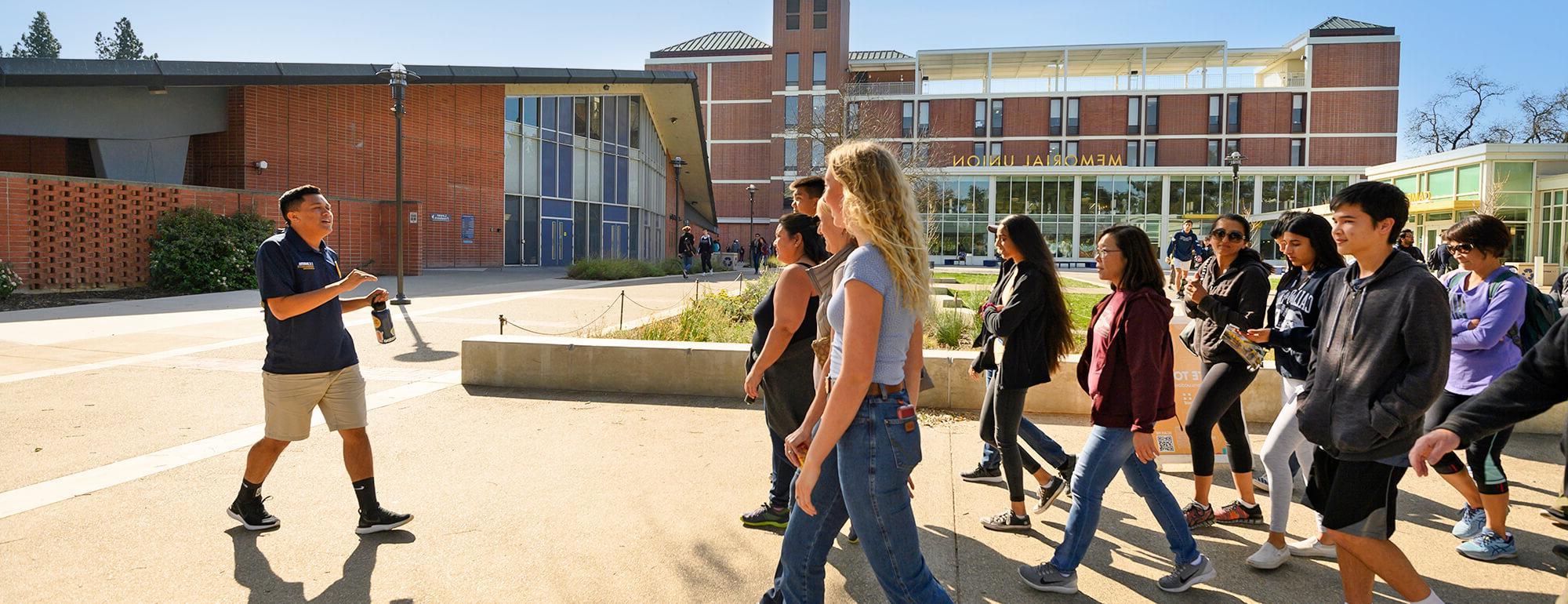 A UC Davis tour guide walks backward through campus highliting campus sights to his audience