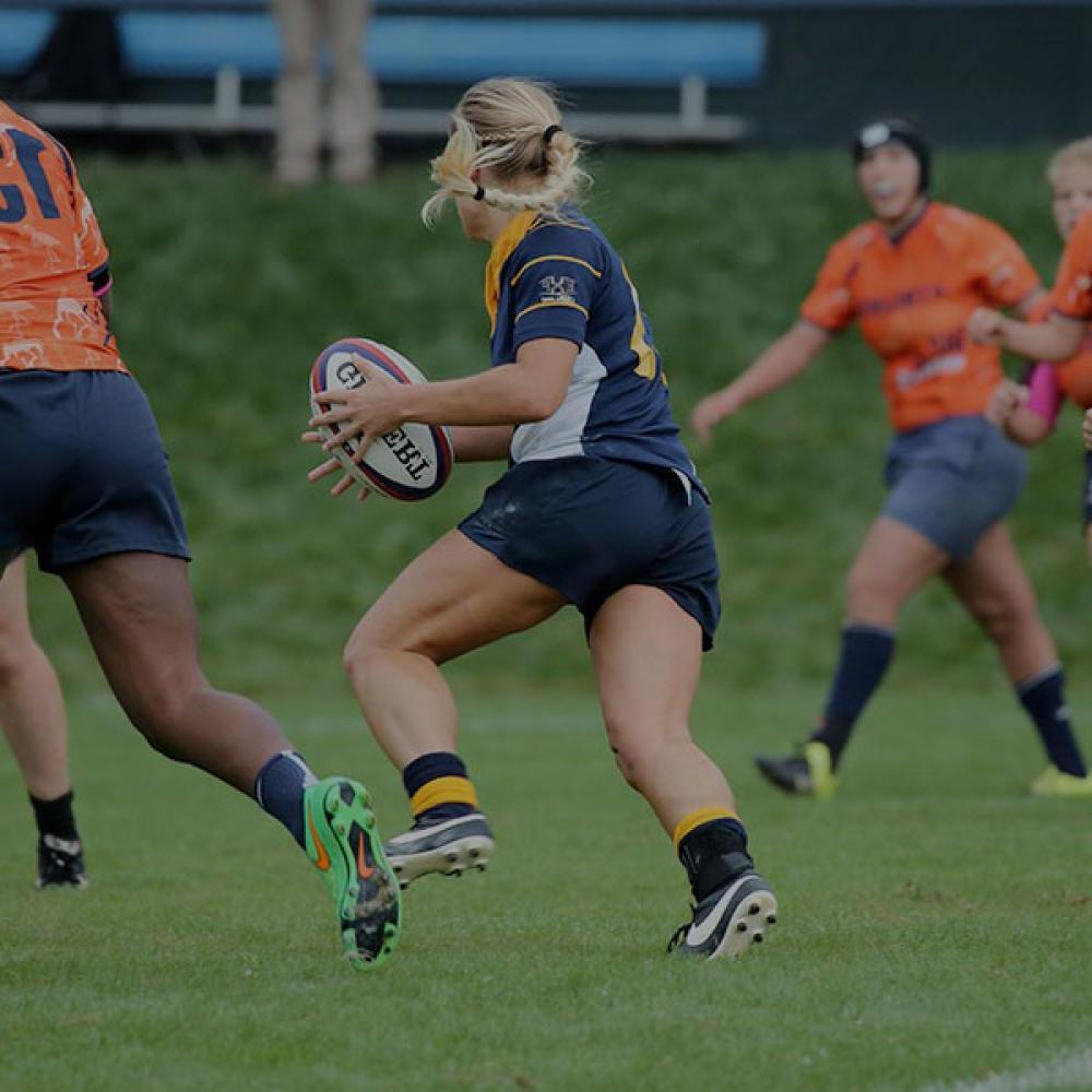 A women's rugby player charges down the field