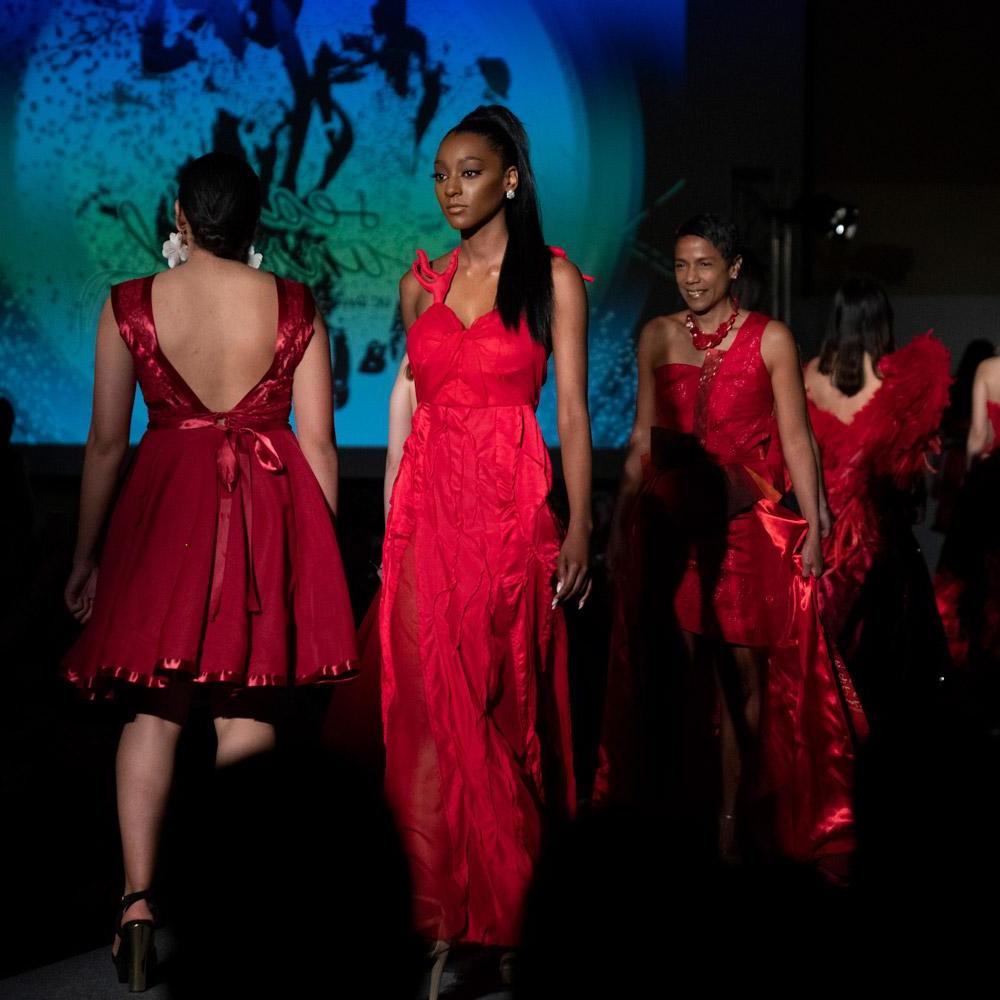 People in red dresses walking down a fashion runway at Picnic Day