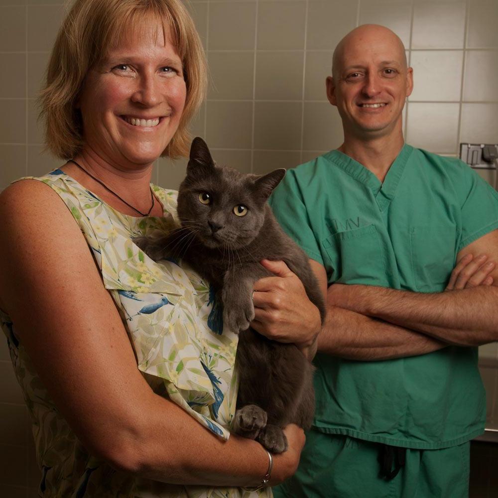 A woman and a veterinarian stand in an office holding a cat