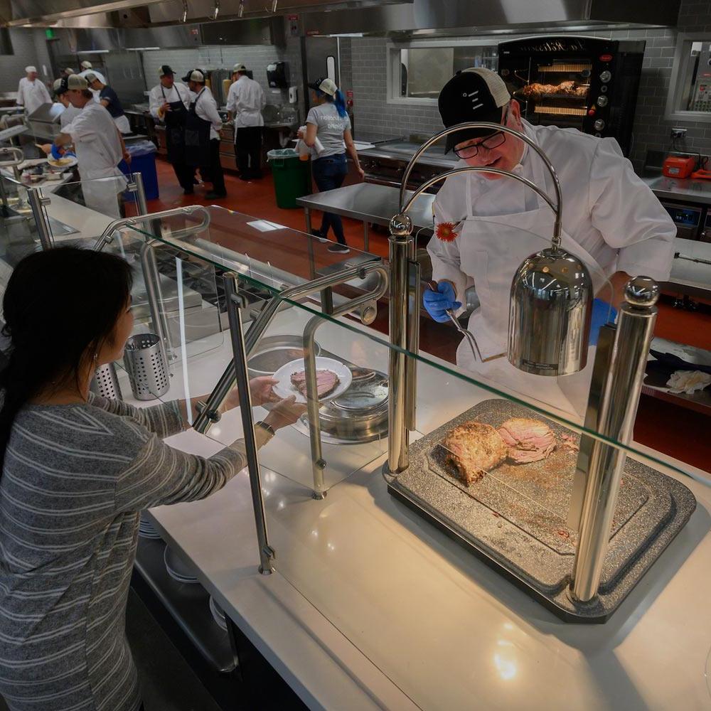 A dining commons employee serves a cut of meat to a UC Davis student
