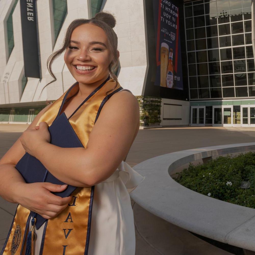 A UC Davis student standing outside of the Golden 1 center holdint their grad regalia